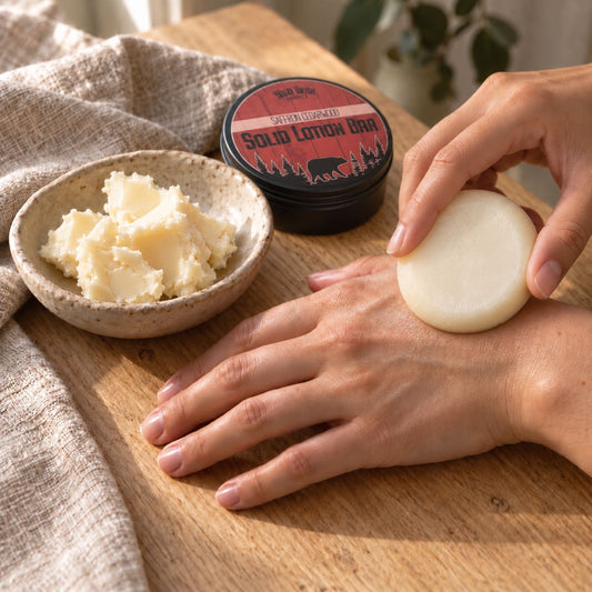 A woman applies a round ivory lotion bar to the back of her hand beside a bowl of shea butter and a Wild Bear Market Saffron Cedarwood tin.