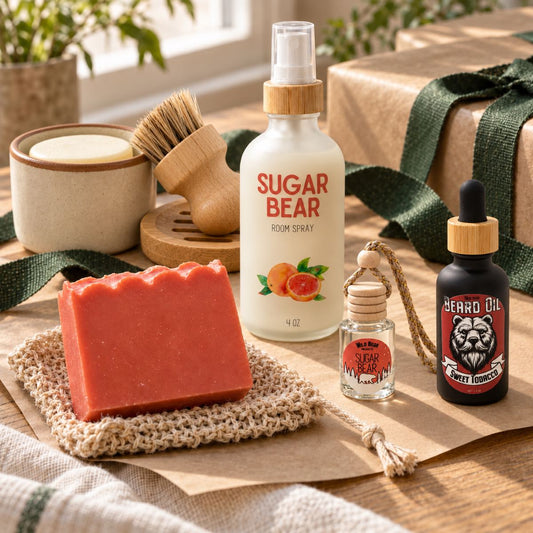 Wild Bear gifts arranged with green ribbon: Sugar Bear soap, room spray and car freshener, a ceramic dish soap jar with wooden brush, and Sweet Tobacco beard oil.
