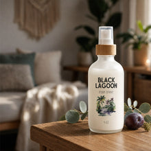 Black Lagoon Room Spray bottle on a wood table in a calm living room with eucalyptus and dark plum